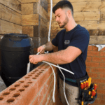 Electrician preparing electrical cable installation beside brick wall
