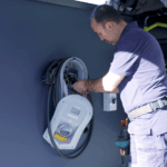Electrician installing home EV charger beside electric vehicle
