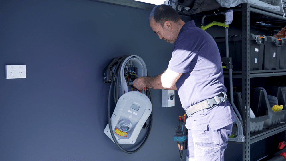 Electrician installing home EV charger beside electric vehicle