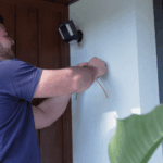 Electrician installing outdoor wall light near residential entrance