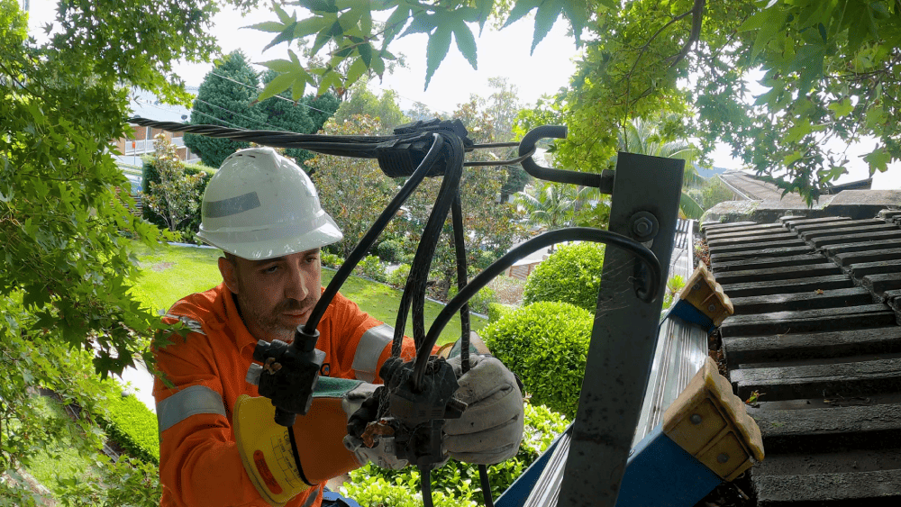 Electrician working on overhead power connection near property roofline