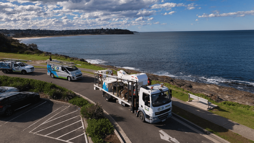 IZCO Electrical fleet and elevated lift truck beside coastal overhead powerline area